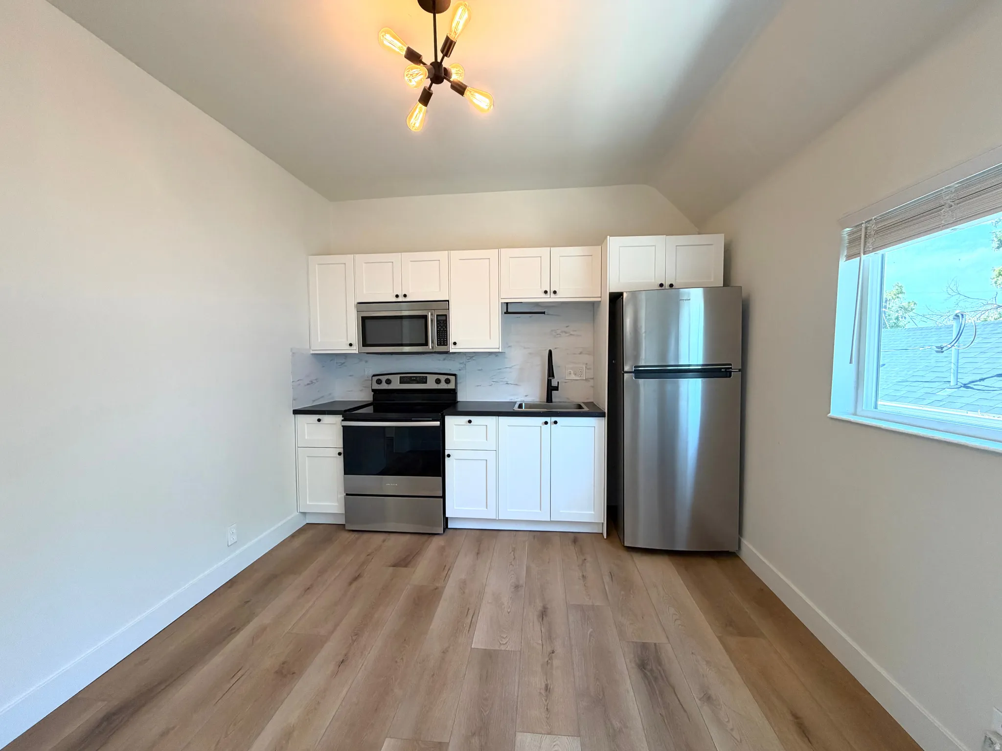 Well-appointed kitchen featuring stainless steel appliances, white cabinetry, dark countertops, and a white tile backsplash