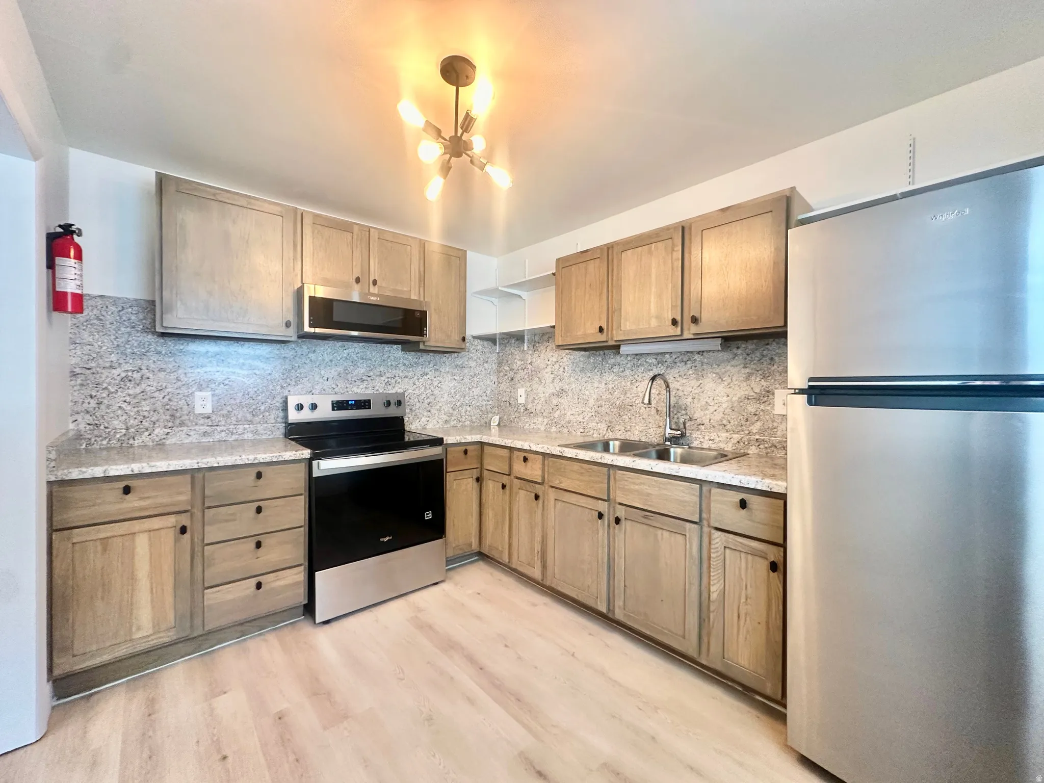 Kitchen featuring light wood-finish cabinetry, light-toned countertops with matching backsplash, stainless steel appliances, and a double basin sink