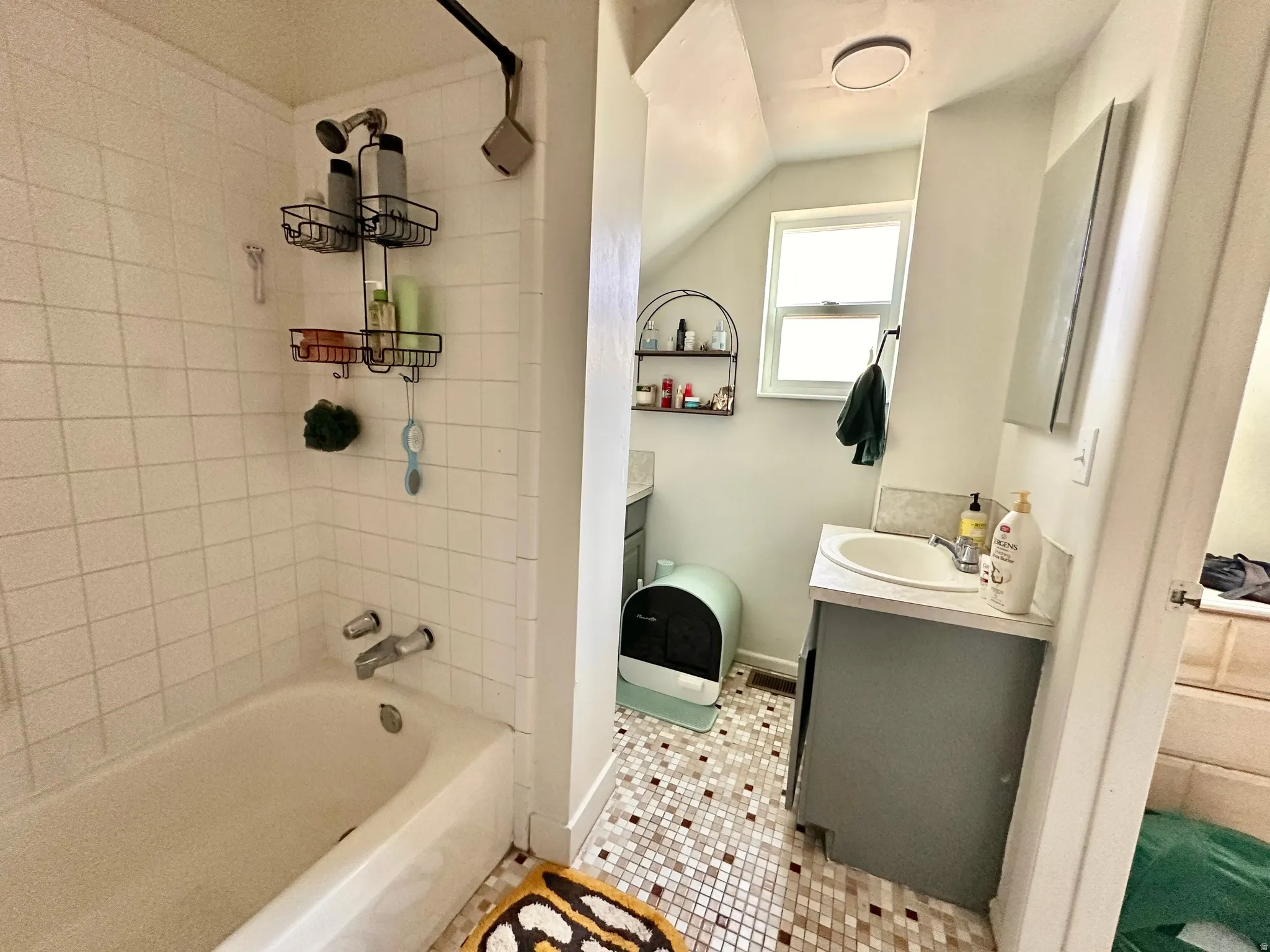 Full bath featuring vanity, shower / bathtub combination, light tile patterned flooring, and vaulted ceiling