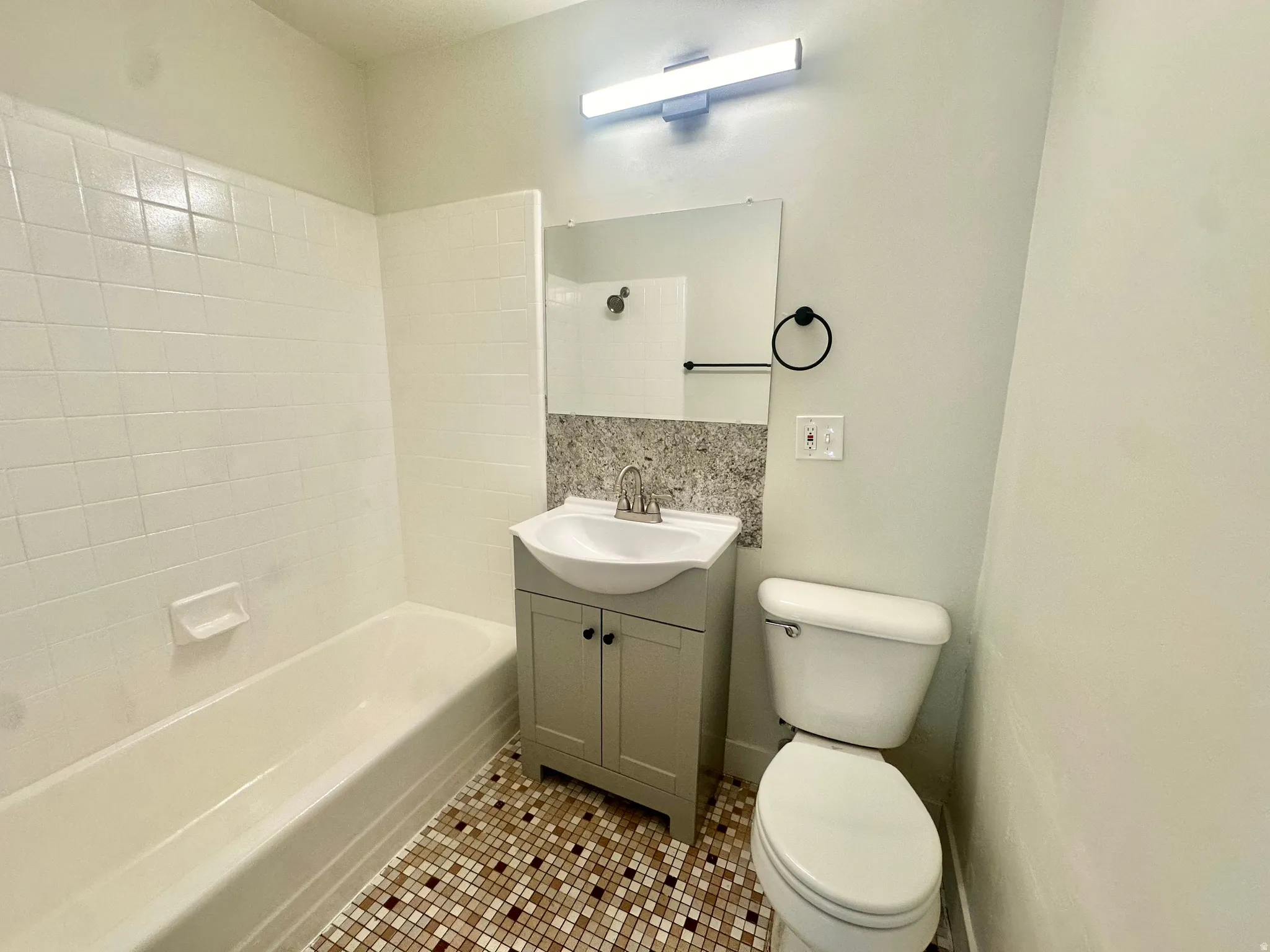 Bathroom featuring a tile-surround bathtub, mosaic tile flooring, a vanity with cabinet storage, a vessel sink, and a wall-mounted mirror with integrated lighting