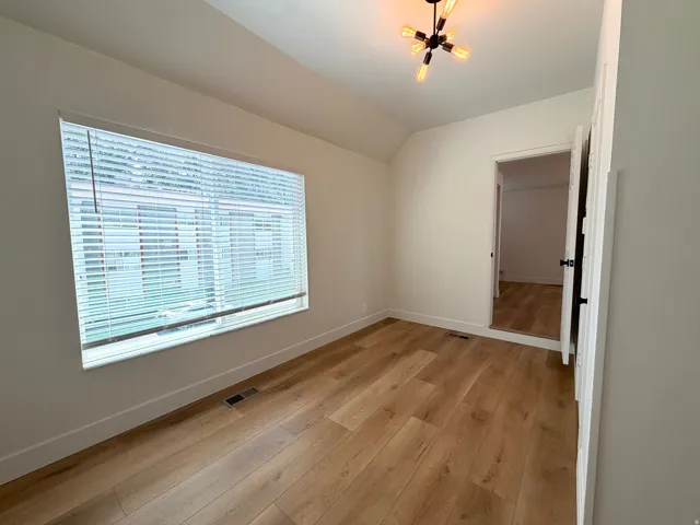 Wood-finish flooring, a large window with blinds, and a modern ceiling light fixture