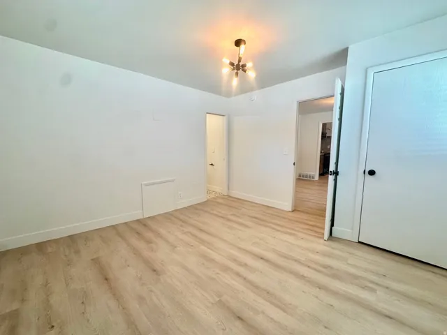 Spacious room featuring wood-finish flooring, crisp white walls, and a contemporary ceiling fixture