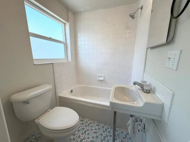 Bathroom featuring a white toilet, white bathtub, white tile shower surround, pedestal sink, and a window