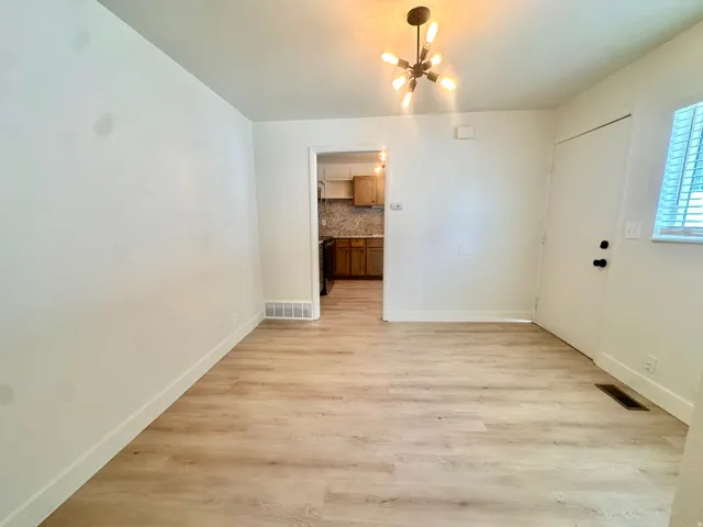 Open-concept area featuring light wood-finish flooring, a contemporary multi-bulb chandelier, white baseboards, and a white interior door with black hardware