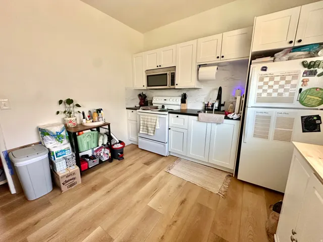 Kitchen featuring white appliances, tasteful backsplash, white cabinets, and light wood finished floors