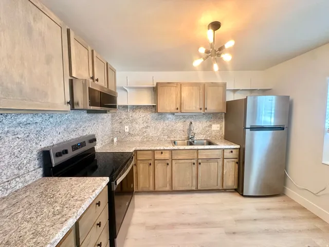 Kitchen featuring light wood-finish cabinetry, granite-style countertops, stainless steel appliances, and wood-finish flooring
