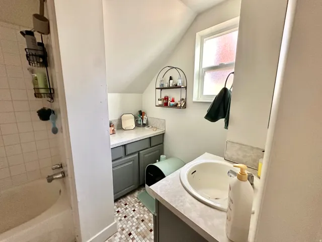 Full bath featuring vanity, bathing tub / shower combination, lofted ceiling, and light tile patterned flooring