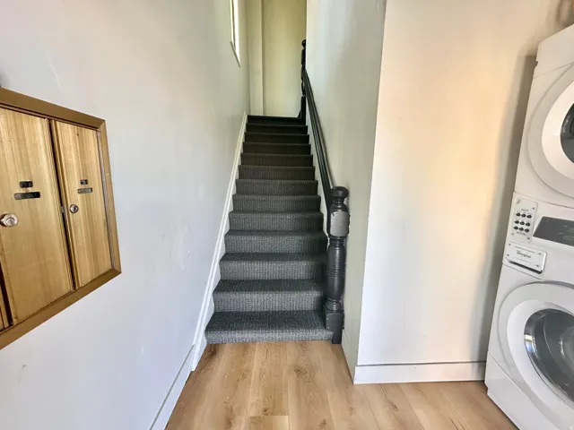 Stairs with wood finished floors and stacked washing machine and dryer