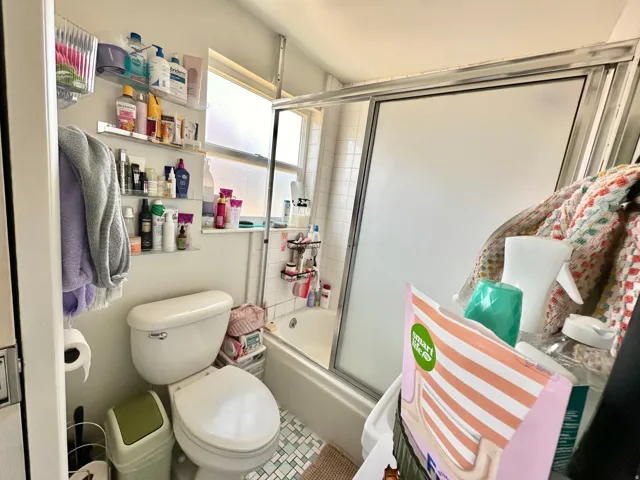 Bathroom with toilet and combined bath / shower with glass door