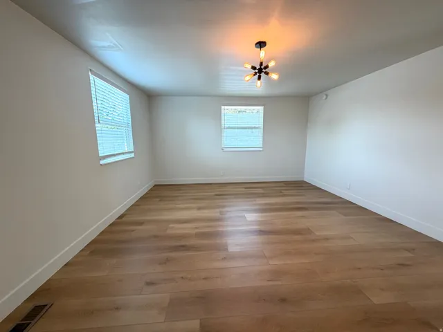 Expansive room featuring wood-finish flooring, multiple windows with blinds, a modern ceiling light fixture, and white wall finishes