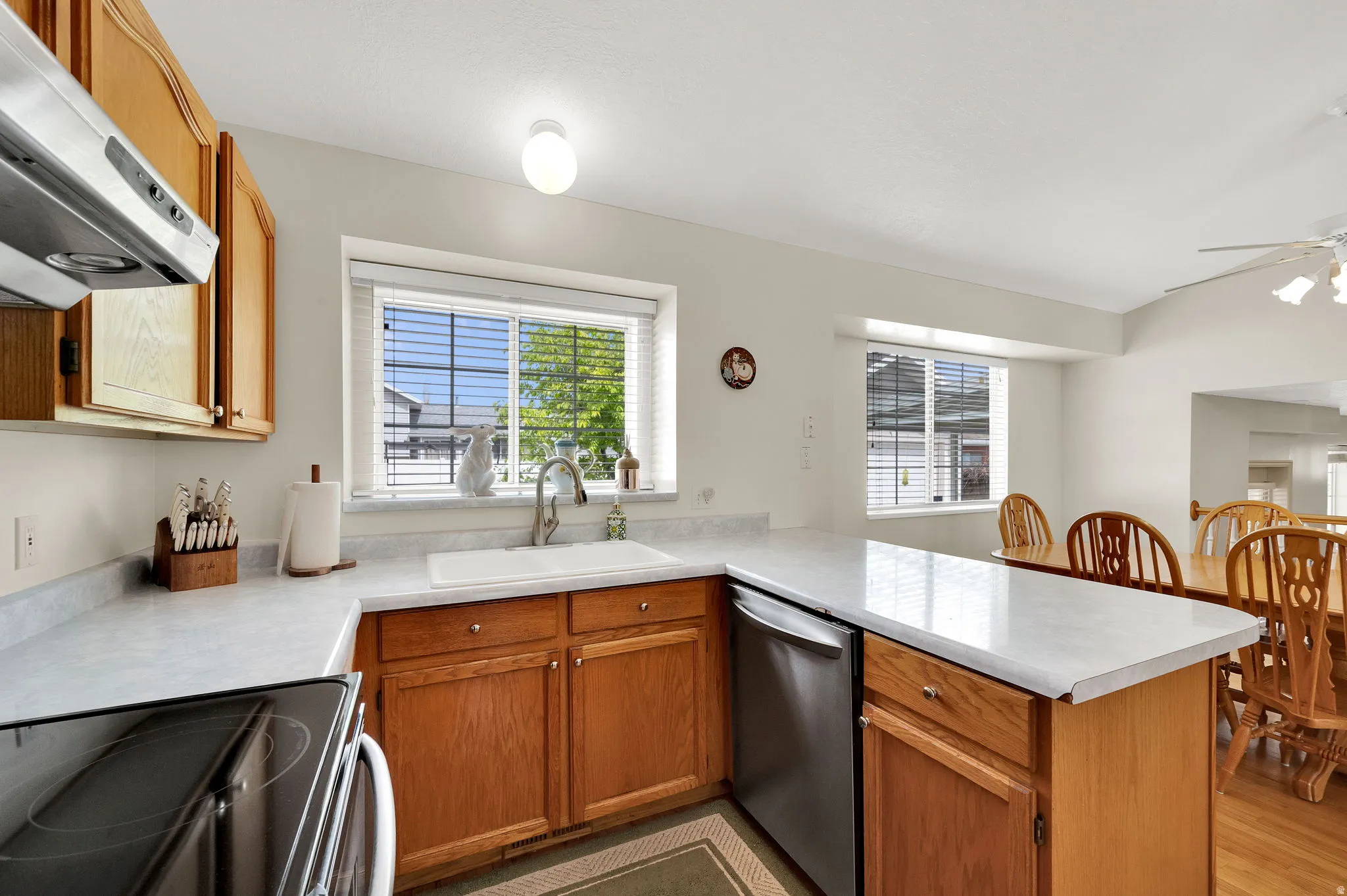 Kitchen with a peninsula, electric stove, light countertops, dishwasher, and wood finish cabinetry