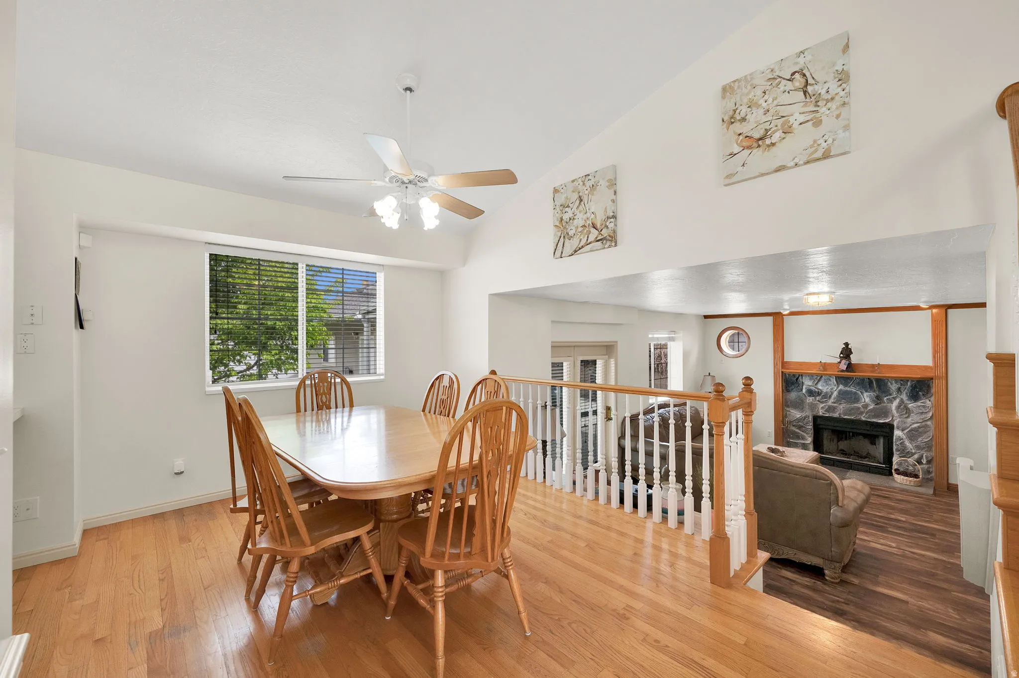 Dining space featuring a stone fireplace, lofted ceiling, light wood-style floors, and a ceiling fan