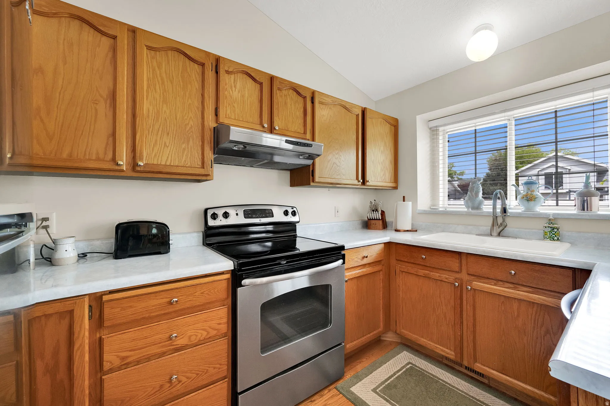 Kitchen with electric range, light countertops, wood finish cabinetry, and vaulted ceiling