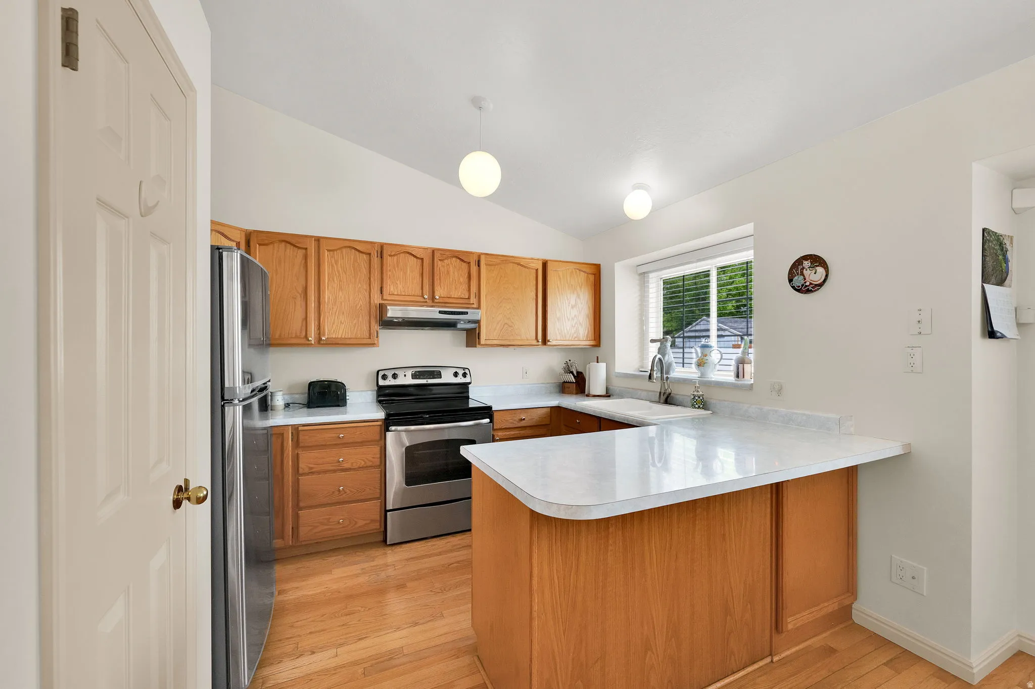 Kitchen featuring a peninsula, stainless steel appliances, vaulted ceiling, wood finish cabinets, and light countertops