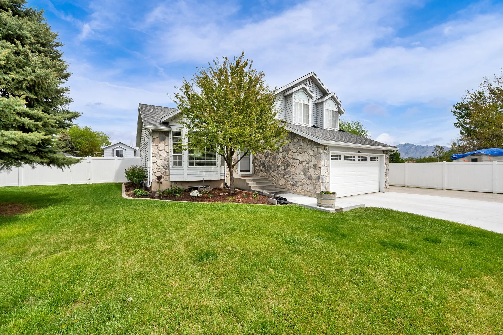 View of property hidden behind natural elements featuring stone siding, concrete driveway, a mountain view, and an attached garage