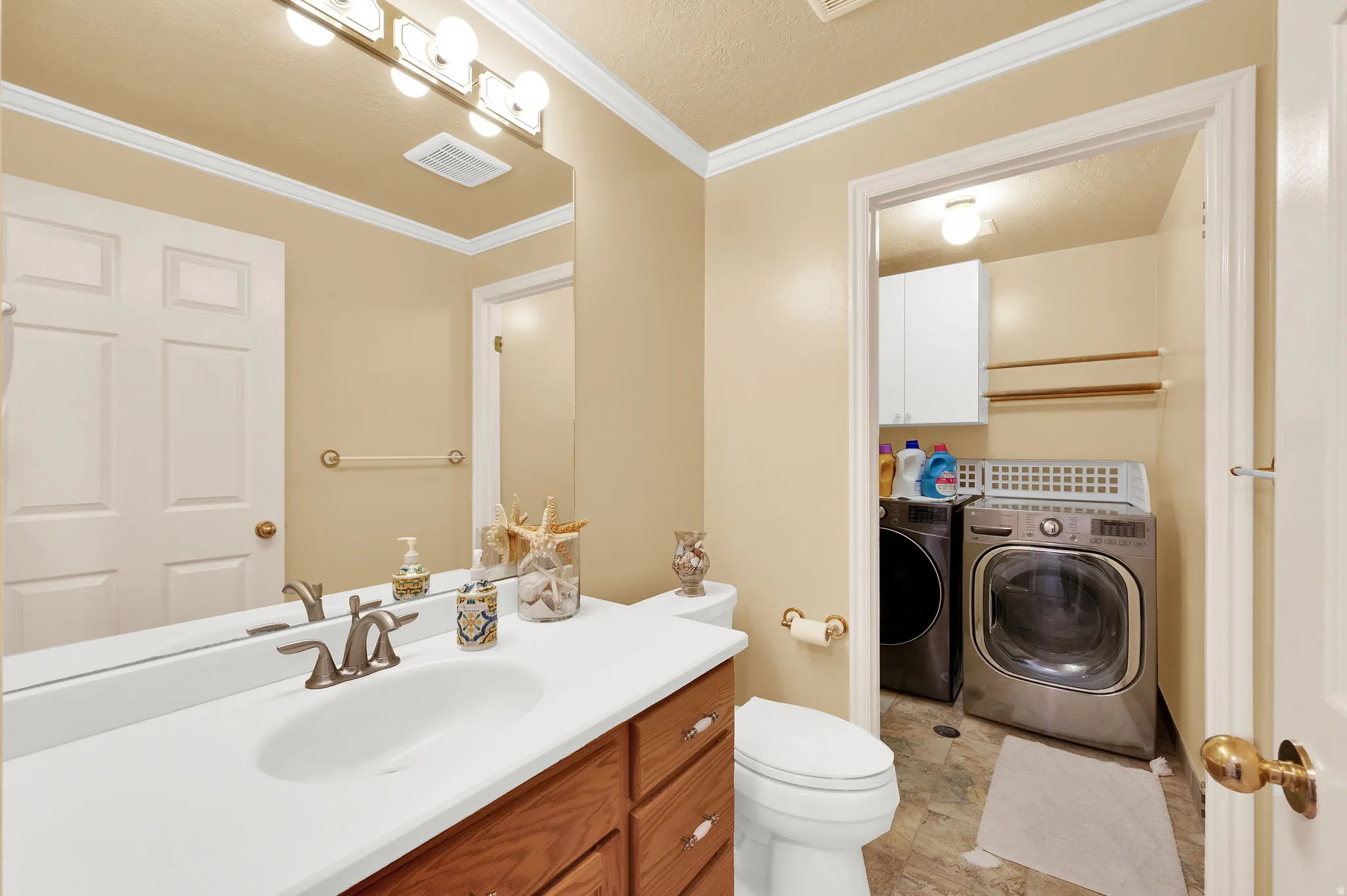 Half bathroom featuring vanity, washing machine and clothes dryer, ornamental molding, and a textured ceiling