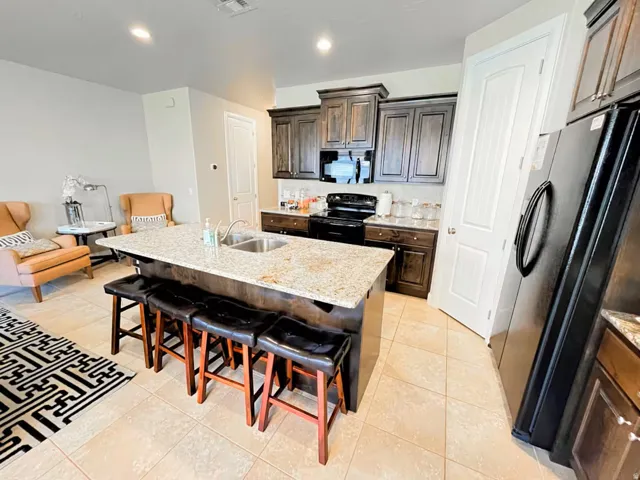 Kitchen with a breakfast bar, black appliances, light stone countertops, a center island with sink, and light tile patterned flooring