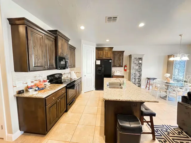 Kitchen featuring black appliances, tasteful backsplash, dark wood finish cabinets, a breakfast bar area, and light stone countertops