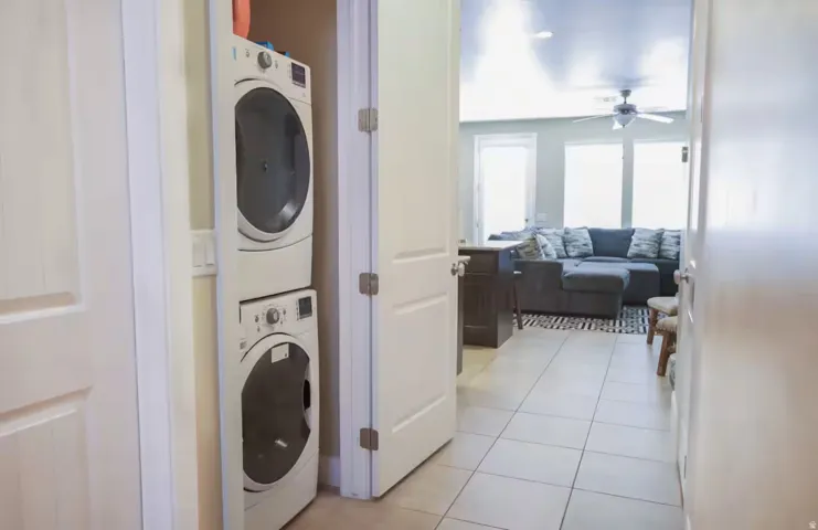 Laundry area featuring light tile patterned flooring, stacked washing machine and dryer, and ceiling fan