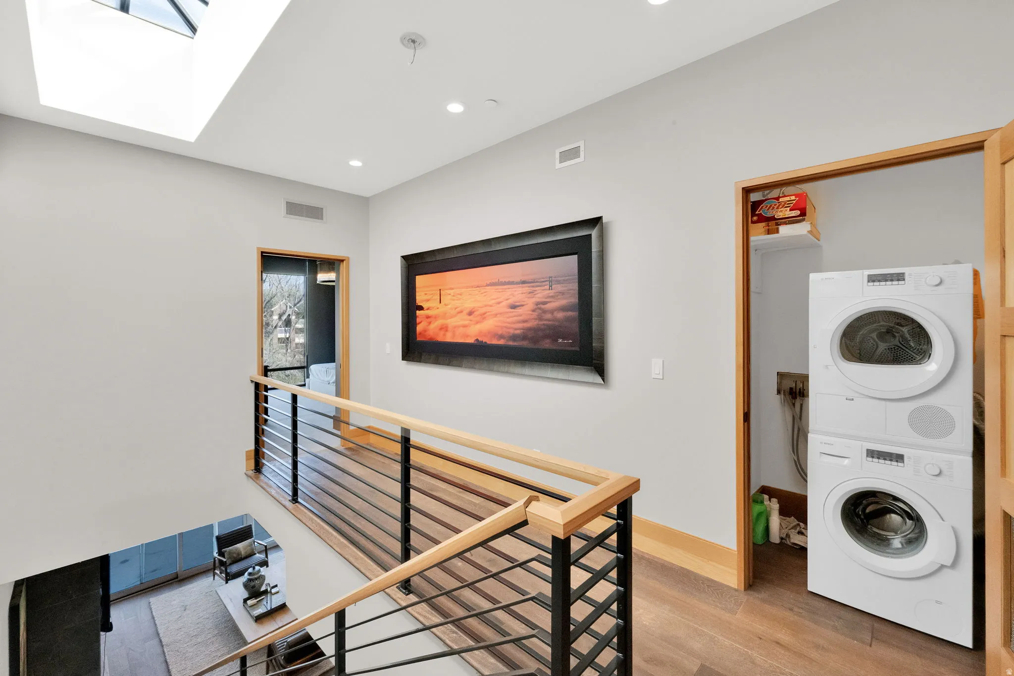 Laundry area featuring light wood-style floors, stacked washer / dryer, a skylight, and recessed lighting