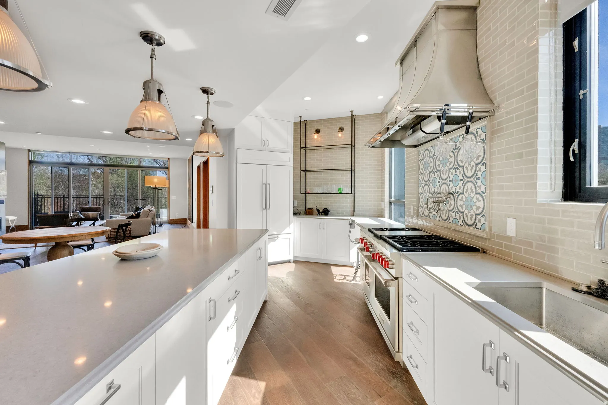 Kitchen featuring high end appliances, ventilation hood, white cabinetry, light wood finished floors, and decorative backsplash