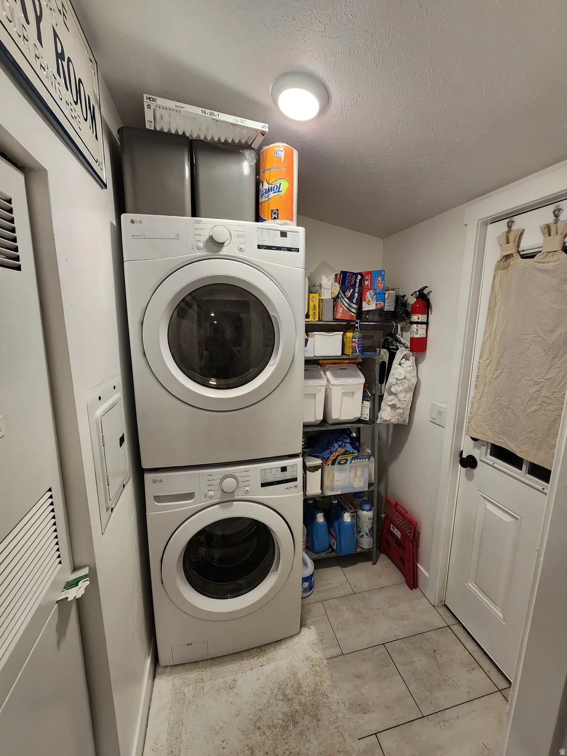 Laundry area featuring a heating unit, stacked washer and dryer, light tile patterned flooring, and a textured ceiling