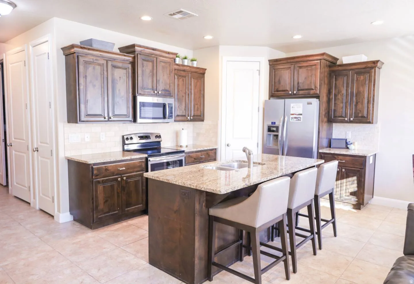 Kitchen featuring stainless steel appliances, light stone countertops, dark wood finish cabinets, backsplash, and recessed lighting
