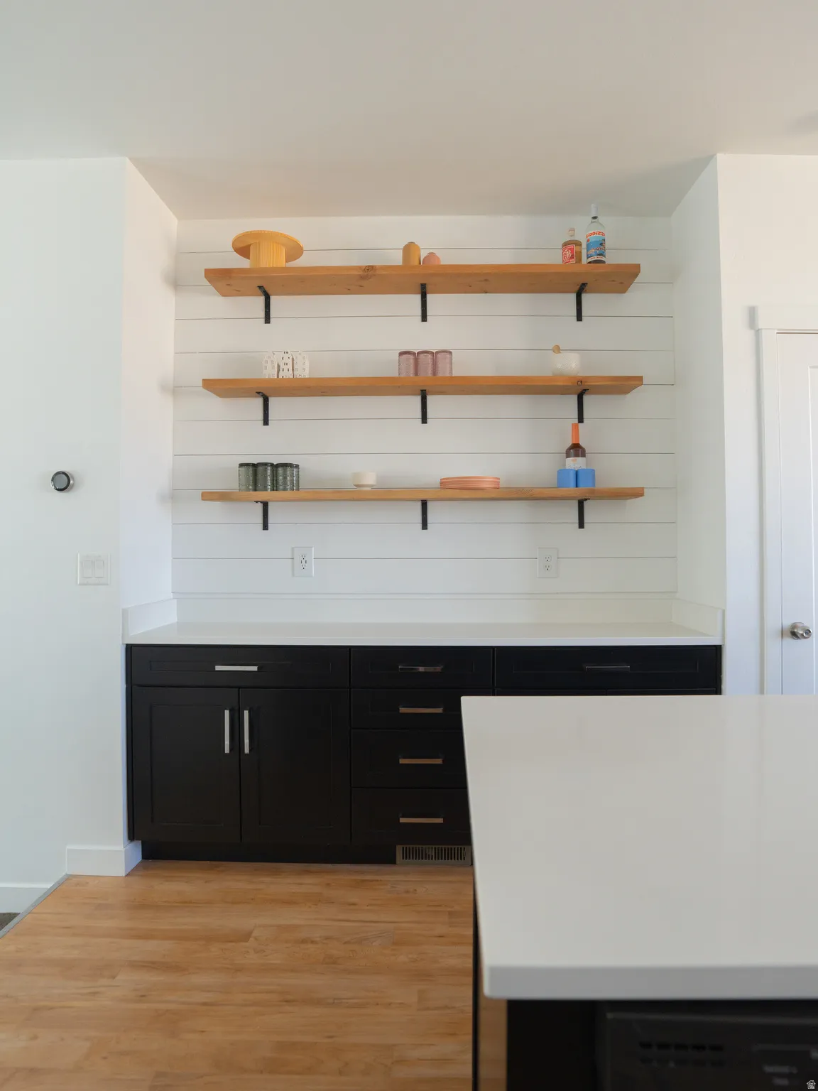 Bar area featuring dark cabinetry, light wood-style floors, and open shelves