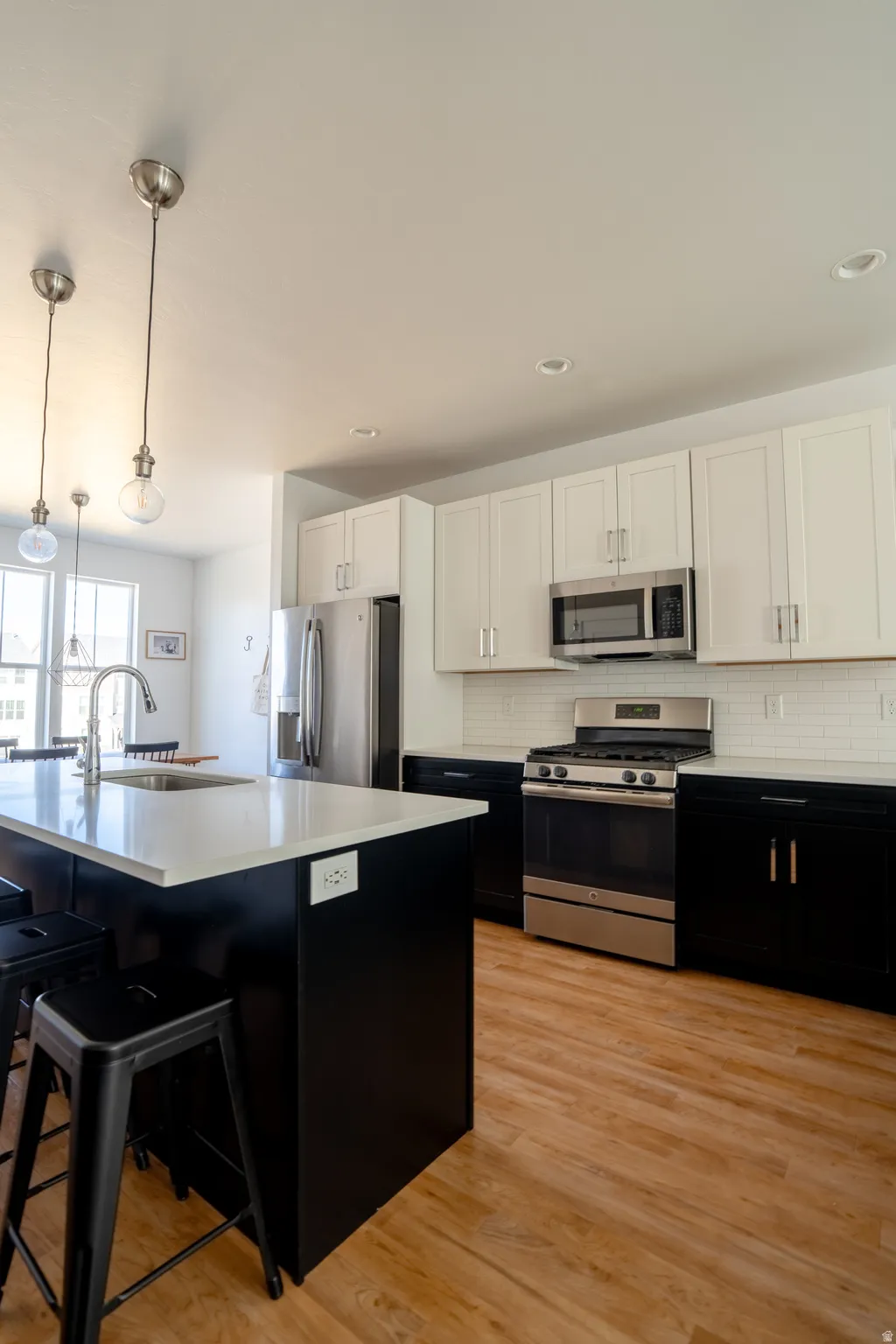 Two tone kitchen featuring two tone color scheme, stainless steel appliances, light wood finished floors, hanging light fixtures, and an island with sink