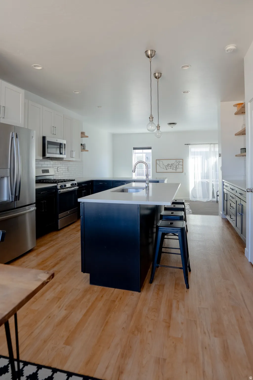 Kitchen with open shelves, two tone cabinetry, stainless steel appliances, pendant lighting, and an island with sink