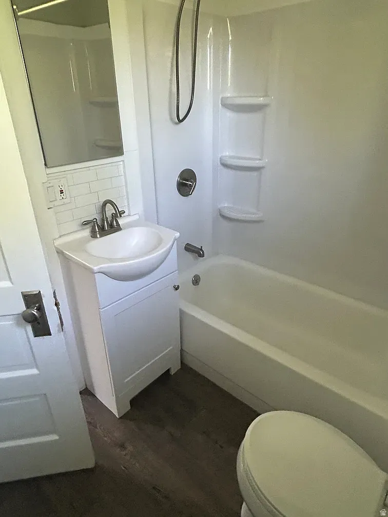 Bathroom with vanity, dark wood-style floors, backsplash, and washtub / shower combination