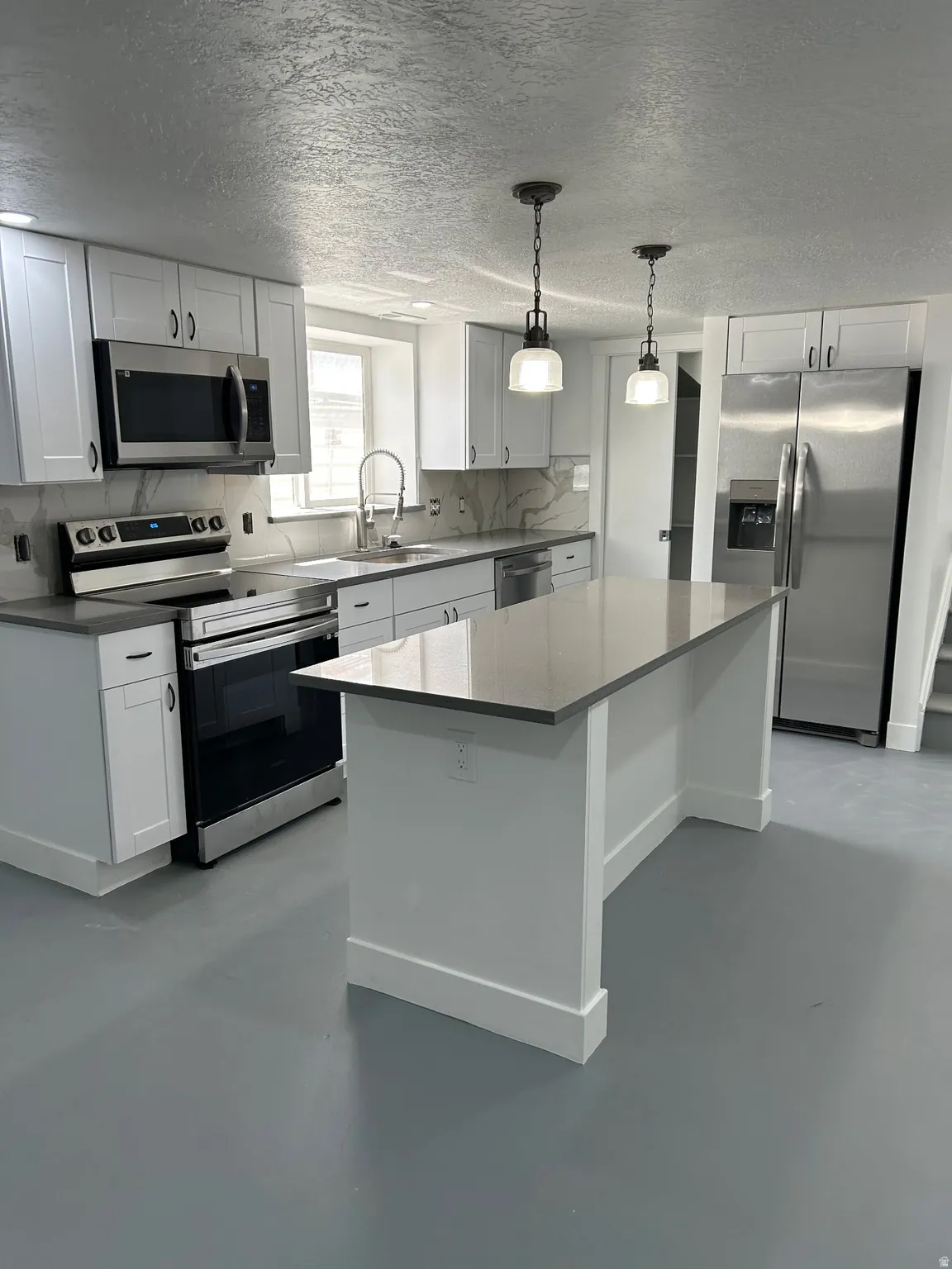 Kitchen with stainless steel appliances, a textured ceiling, pendant lighting, white cabinets, and finished concrete floors