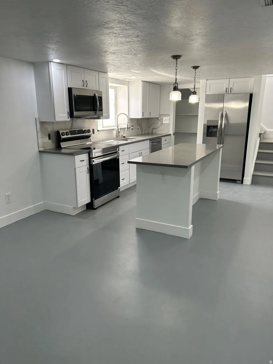 Kitchen featuring stainless steel appliances, decorative backsplash, white cabinets, a textured ceiling, and concrete flooring