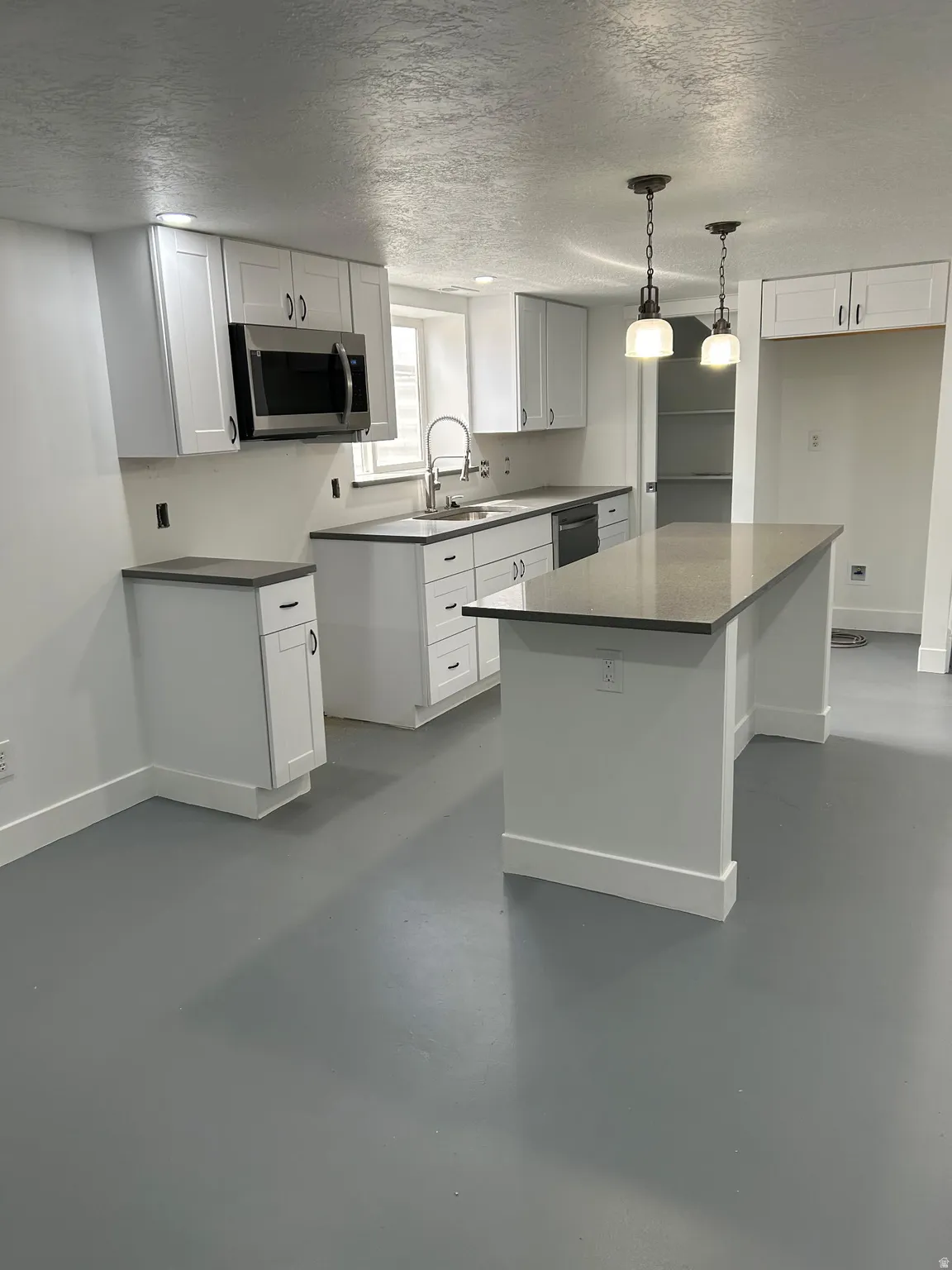 Kitchen with finished concrete floors, a textured ceiling, stainless steel appliances, white cabinetry, and a kitchen island