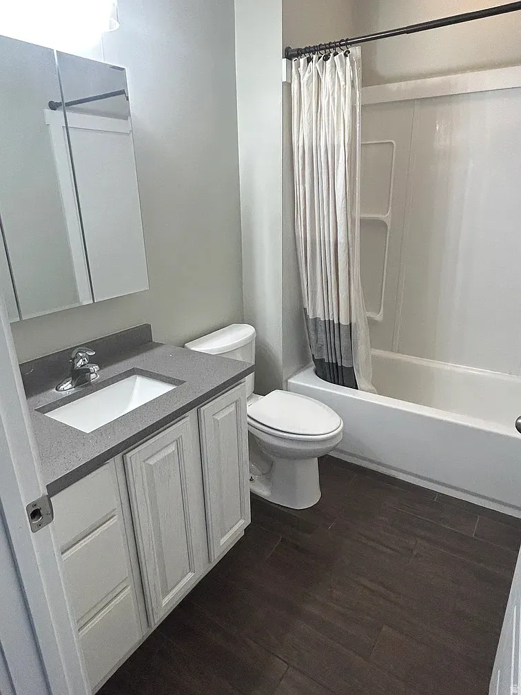 Full bath featuring vanity, shower / tub combo with curtain, and dark wood-style floors