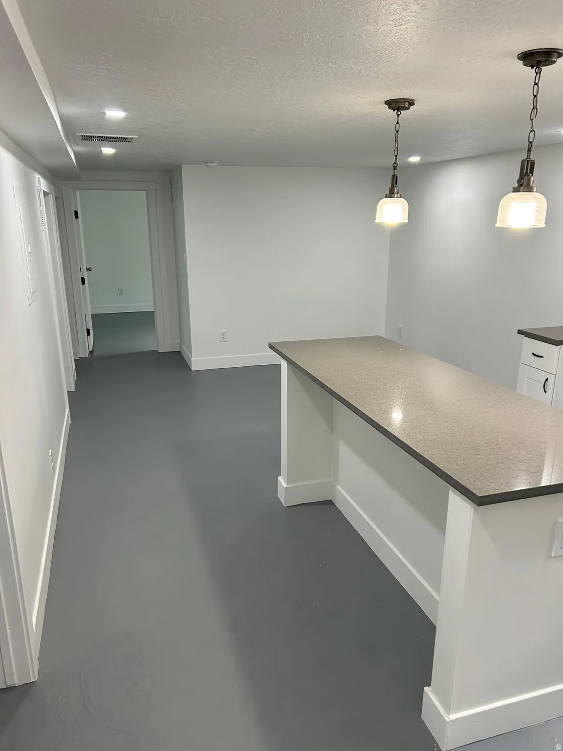 Kitchen featuring pendant lighting, a textured ceiling, concrete flooring, white cabinets, and a kitchen island