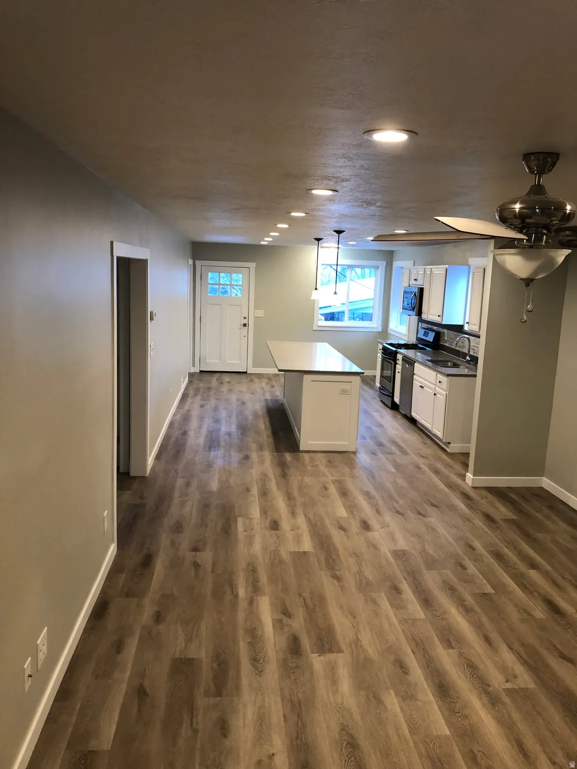 Kitchen featuring white cabinetry, dark countertops, stainless steel appliances, decorative light fixtures, and a kitchen island