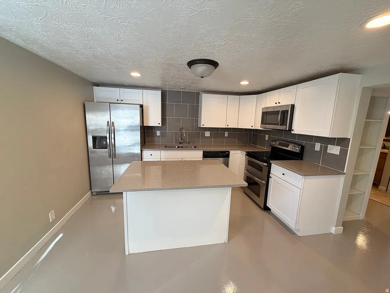 Kitchen featuring stainless steel appliances, finished concrete flooring, white cabinets, tasteful backsplash, and recessed lighting