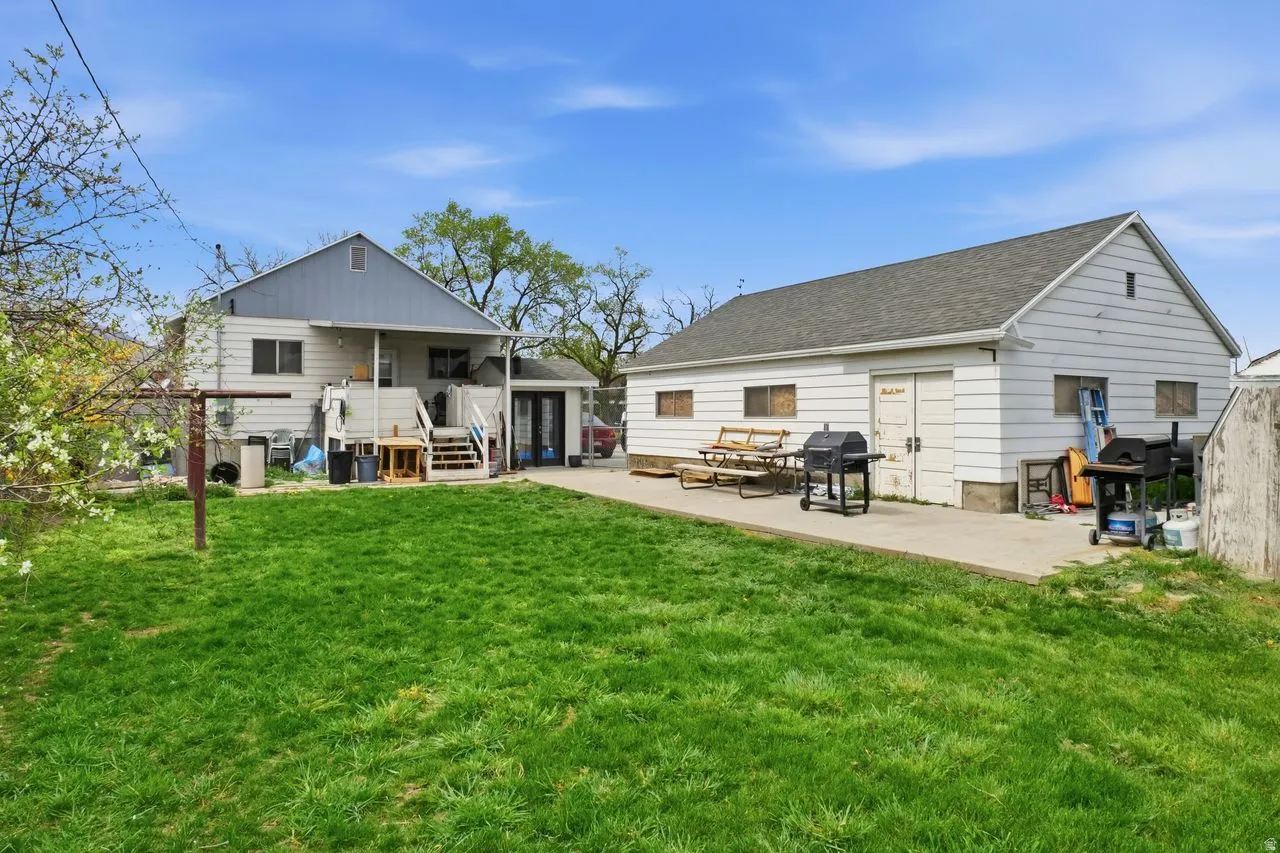 Back of property featuring a patio area, a lawn, an outdoor structure, a shingled roof, and board and batten siding
