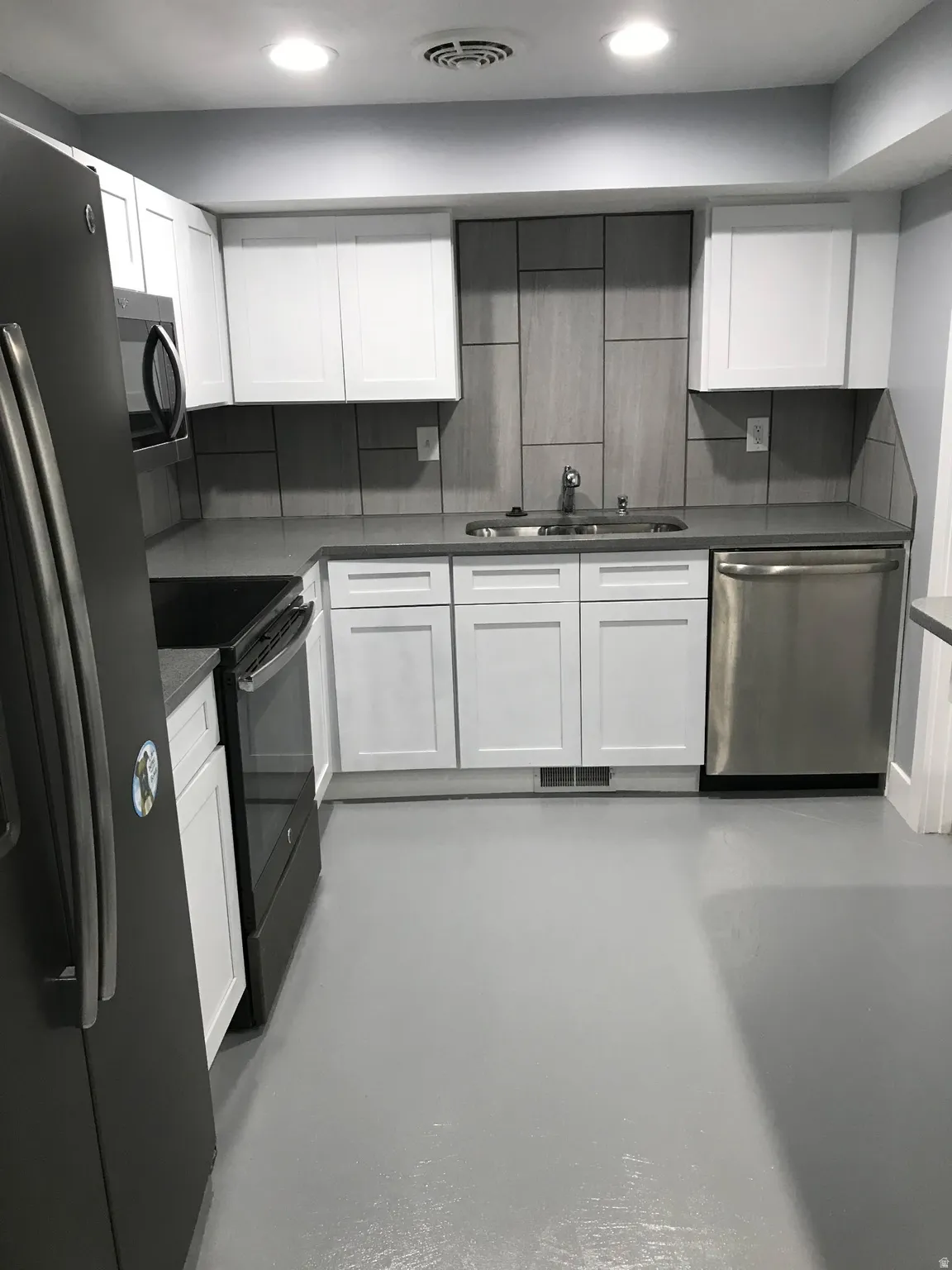 Kitchen with white cabinets, black appliances, concrete floors, dark stone countertops, and recessed lighting