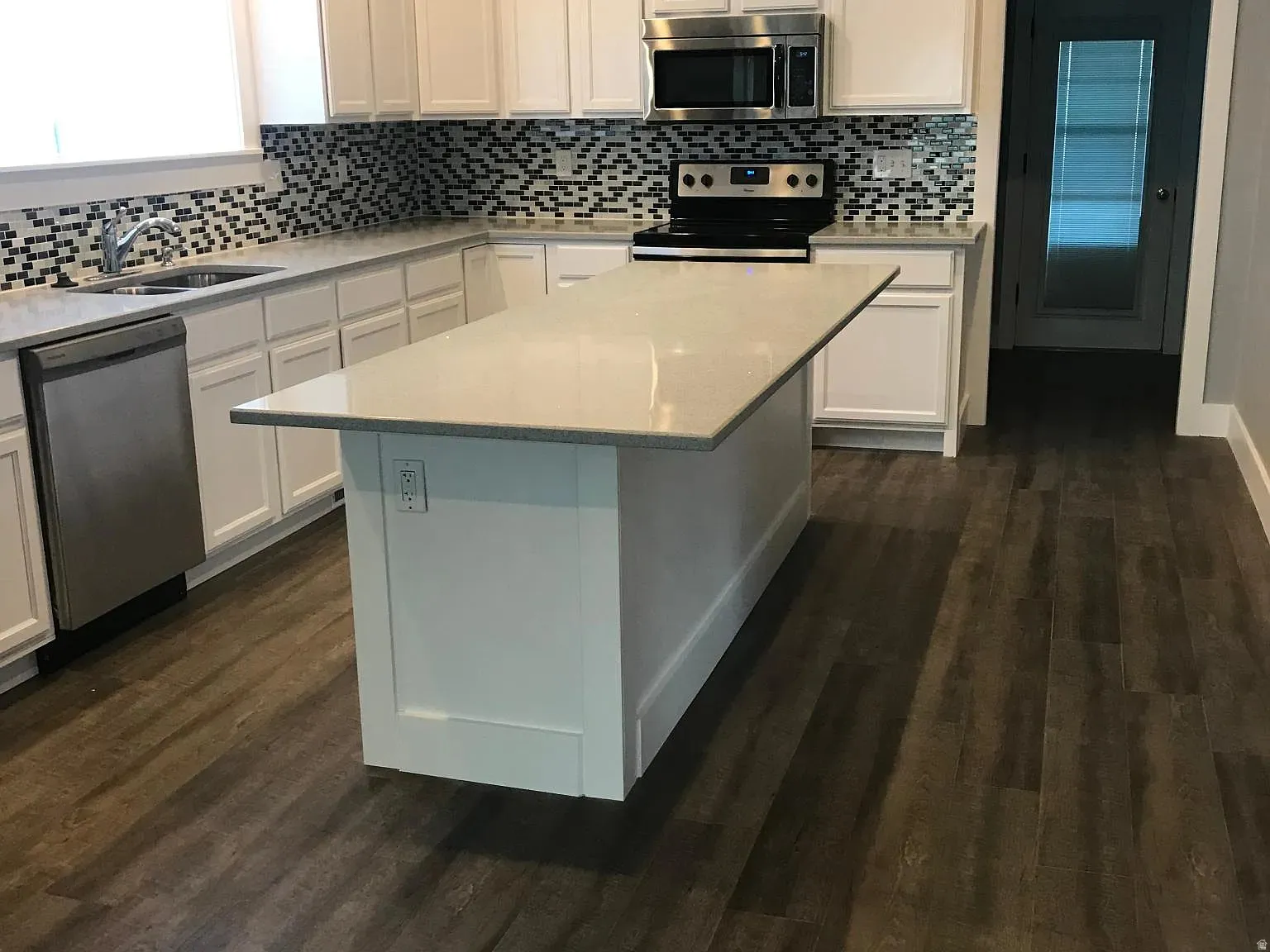 Kitchen with stainless steel appliances, dark wood-type flooring, white cabinetry, and light stone counters