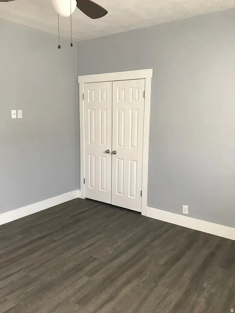 Unfurnished bedroom with dark wood-style flooring, a closet, and a ceiling fan
