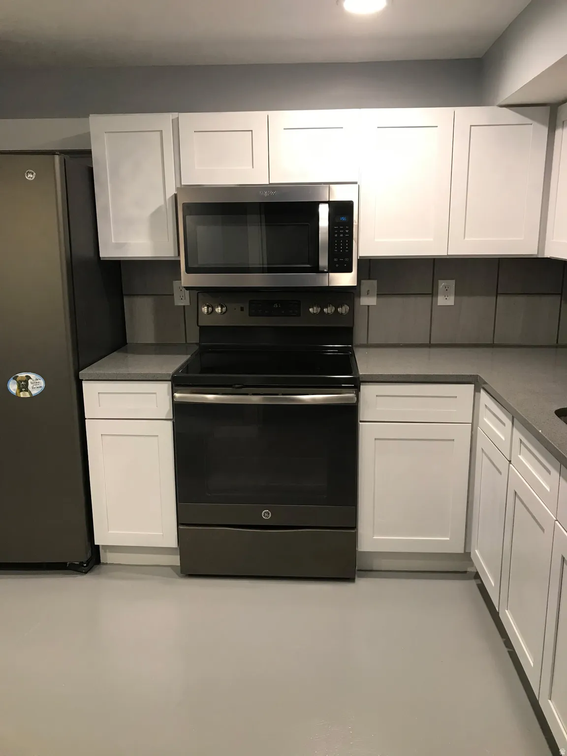 Kitchen with stainless steel appliances, white cabinetry, and finished concrete flooring