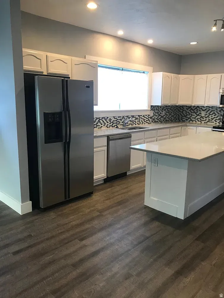 Kitchen featuring stainless steel appliances, tasteful backsplash, white cabinets, dark wood finished floors, and a center island