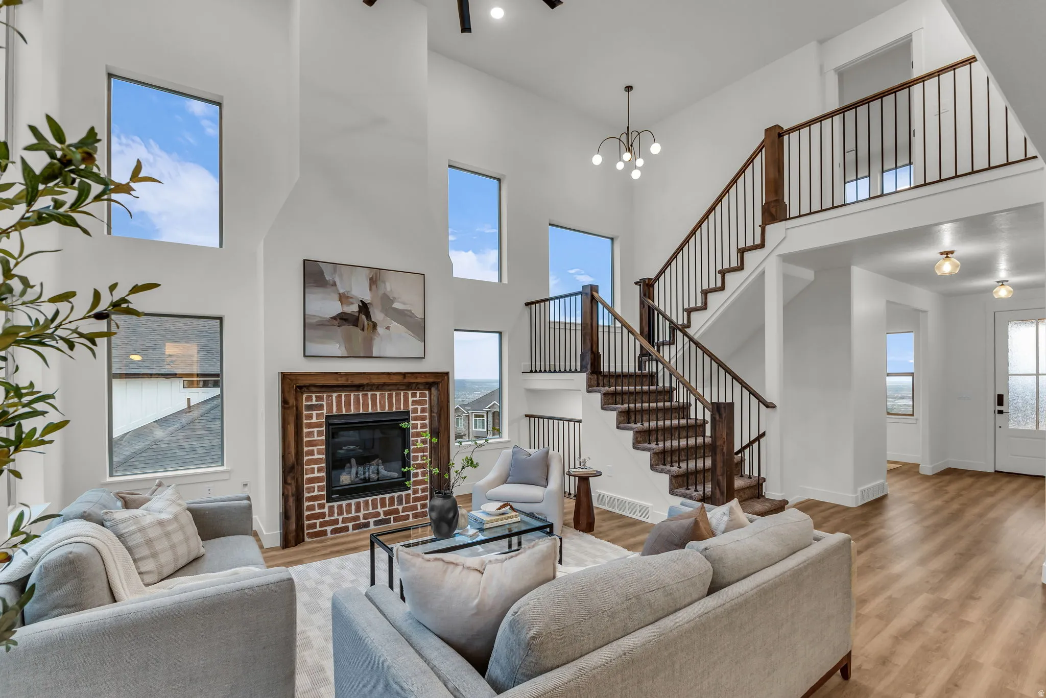 Living area featuring a high ceiling, light wood-type flooring, a brick fireplace, a chandelier, and healthy amount of natural light