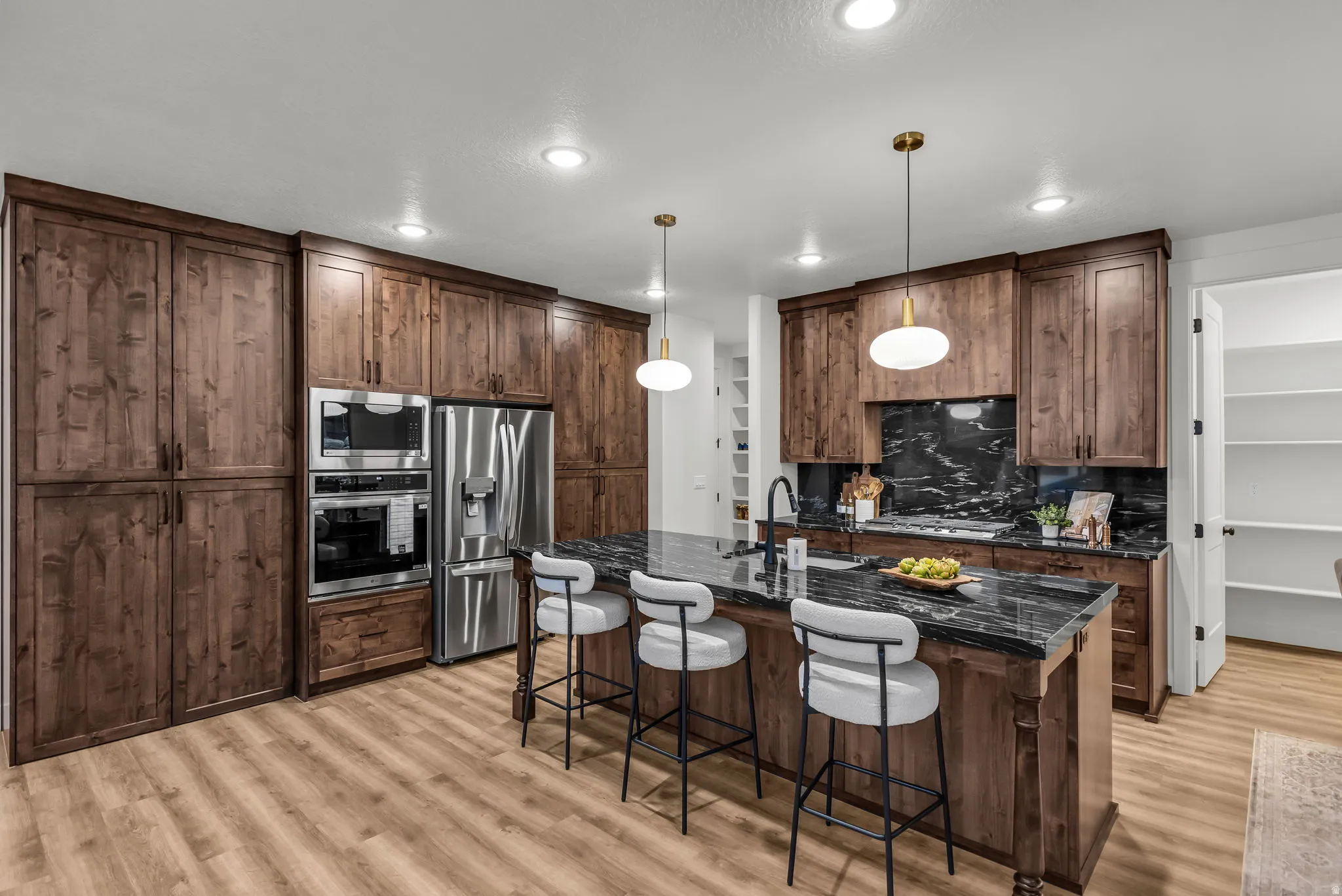 Kitchen with a kitchen bar, stainless steel appliances, decorative light fixtures, a center island with sink, and dark stone counters