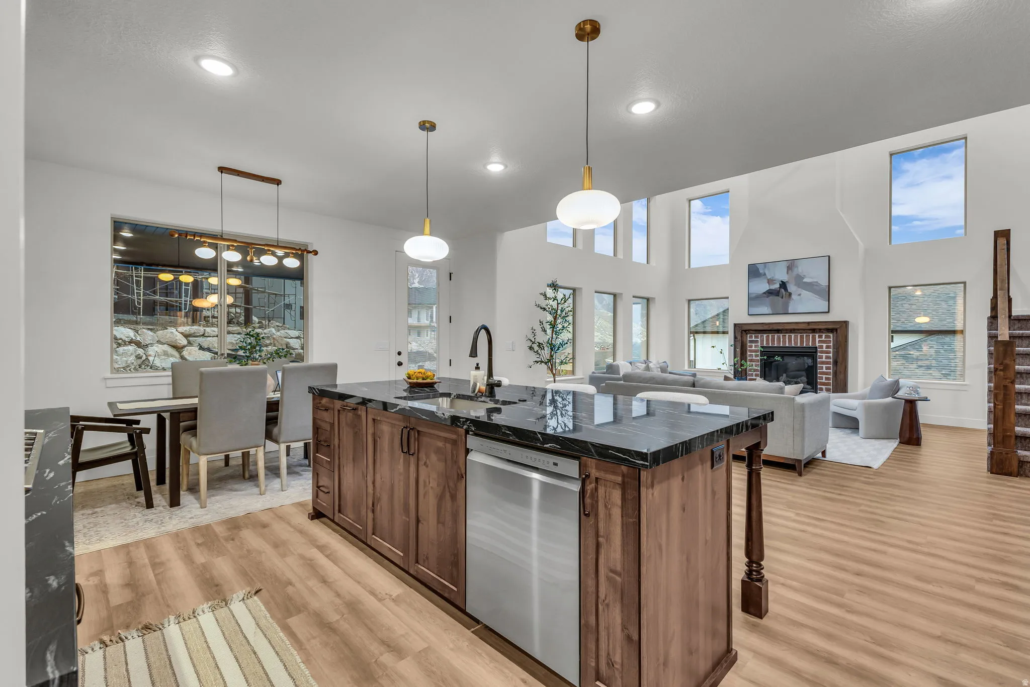Kitchen with an island with sink, a fireplace, dishwasher, decorative light fixtures, and a high ceiling