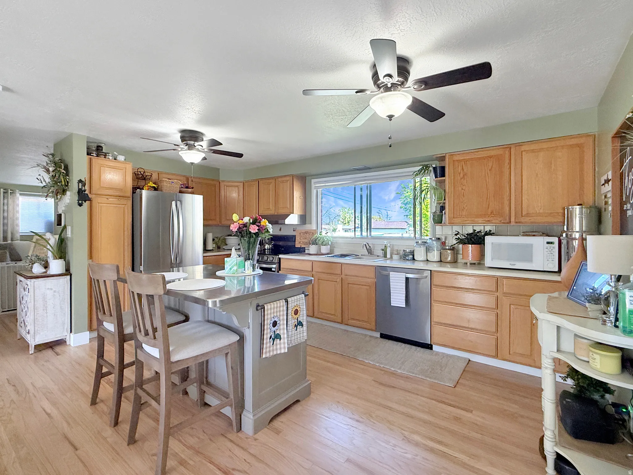 Kitchen featuring light countertops, stainless steel appliances, ceiling fan, light wood finished floors, and a textured ceiling