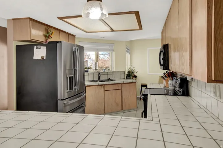 Kitchen with tile counters, black appliances, decorative backsplash, and a ceiling fan