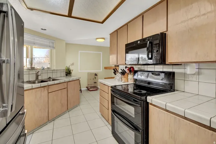Kitchen featuring black appliances, tile countertops, tasteful backsplash, and light tile patterned flooring